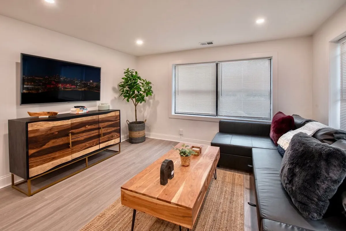 A cozy living room scene featuring a black leather sofa, wooden coffee table, decorative plant, and TV unit. Natural light and comfortable seating make the area inviting for studying, relaxing, or socializing before heading out to explore the nearby university or museums.