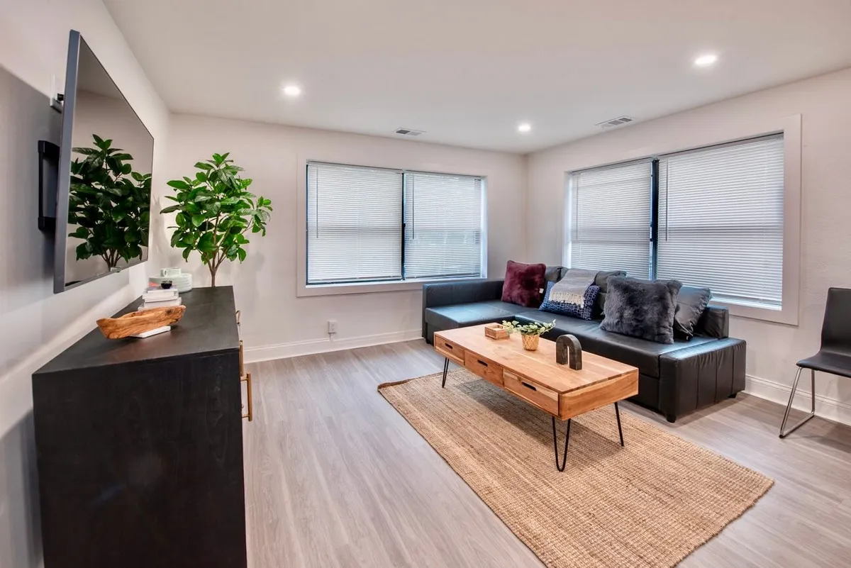 This image showcases a cozy and contemporary living room with a stylish sofa, modern coffee table, a television, and lush green plant accents. The space is brightened by natural lighting and arranged for both relaxation and socializing, perfectly embodying a welcoming urban hub.