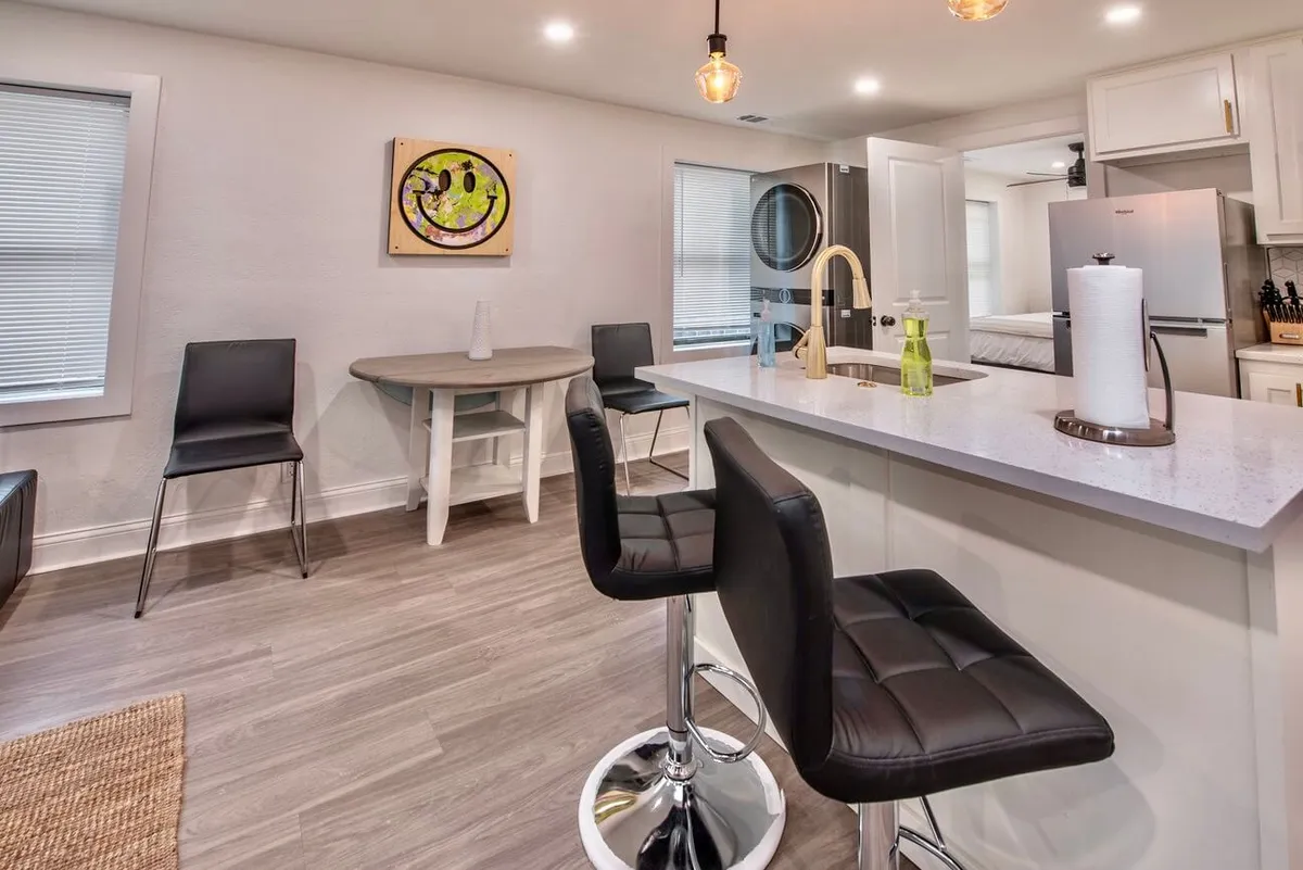 A modern kitchen island with sleek bar stools, complemented by colorful artwork and open sight lines to adjacent living areas. The space is filled with inviting light and arranged for both socializing and casual dining.