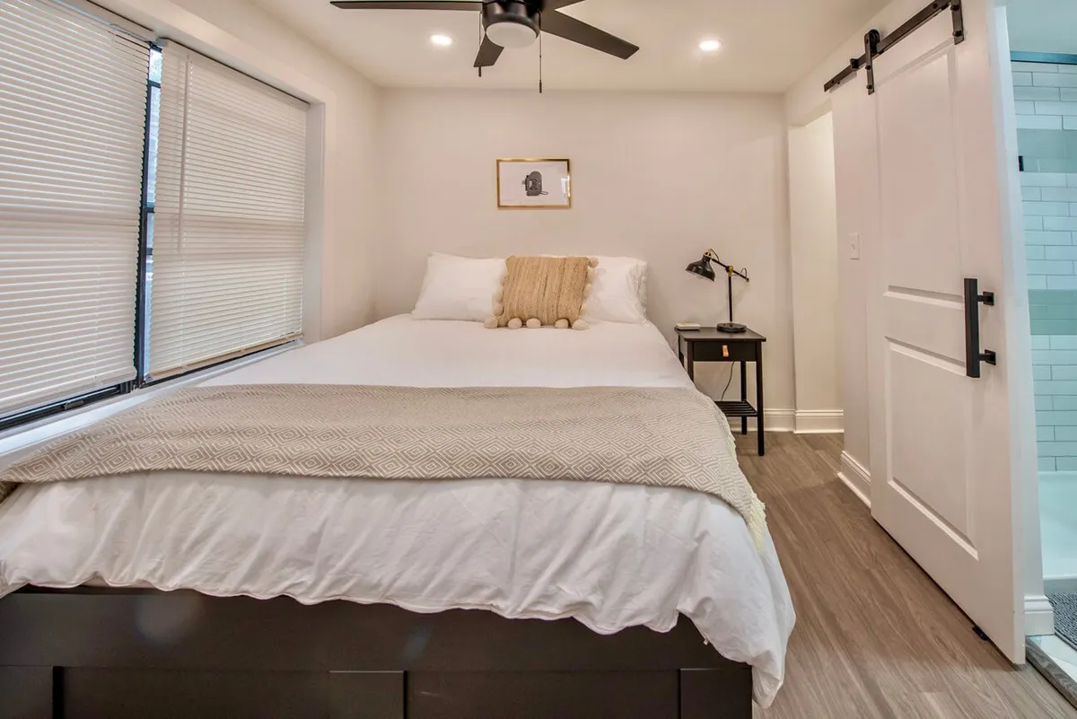 A cozy bedroom featuring a neatly made bed with soft linens, a decorative wall frame adding a touch of personality, and a nightstand providing space for evening reading or a morning coffee. Natural light filters in, enhancing the inviting and restful atmosphere.